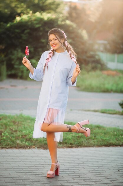 Chica de positividad de moda en vestido azul posando con corazón de caramelo.