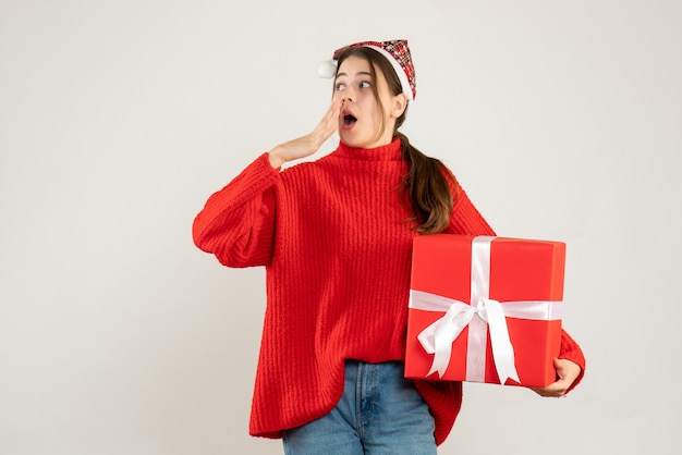 Chica preguntando con gorro de Papá Noel sosteniendo el dedo actual poniendo la mano en la cara en blanco