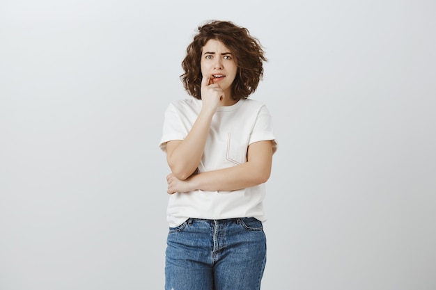 Chica preocupada mordiendo el dedo y luciendo nerviosa, pensando demasiado