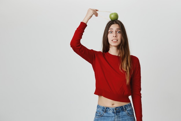 Chica preocupada con objetivo de manzana en la cabeza, apretar los dientes alarmados