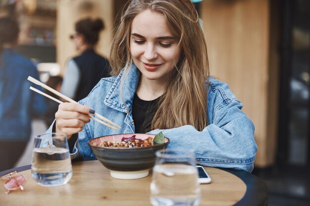 Chica probando comida asiática por primera vez apoyándose en la mesa mientras st