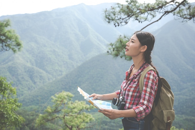 La chica se puso de pie para ver el mapa en la cima de una colina en un bosque tropical junto con mochilas en el bosque. Aventura, senderismo.