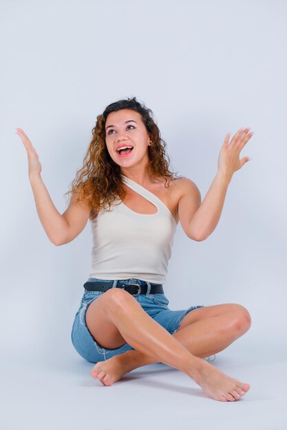 La chica que ríe está mirando hacia arriba levantando las manos sobre fondo blanco.