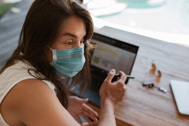 Chica que trabaja en la computadora portátil en una máscara. Foto de alta calidad