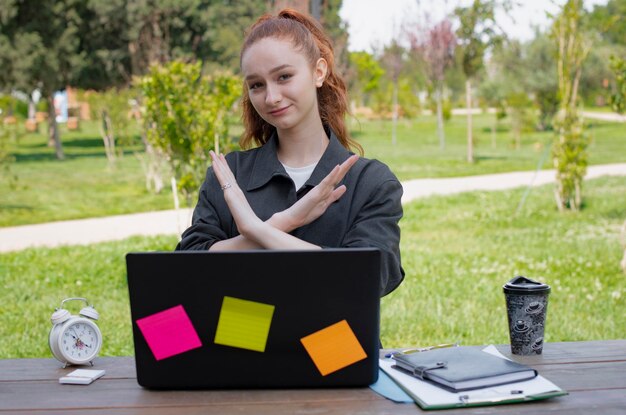 Chica que trabaja en la computadora portátil que muestra dejar de cruzar las manos al aire libre