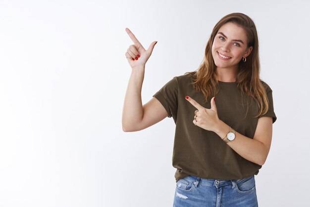 Chica quiere que hagas clic. Retrato lindo atractivo femenino joven alta mujer vistiendo camiseta casual inclinando la cabeza coqueta sonriendo dientes blancos apuntando a la esquina superior izquierda sugiriendo el uso del servicio, mira promo