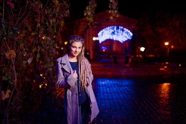 Chica con rastas caminando por la calle nocturna de la ciudad contra luces de guirnaldas