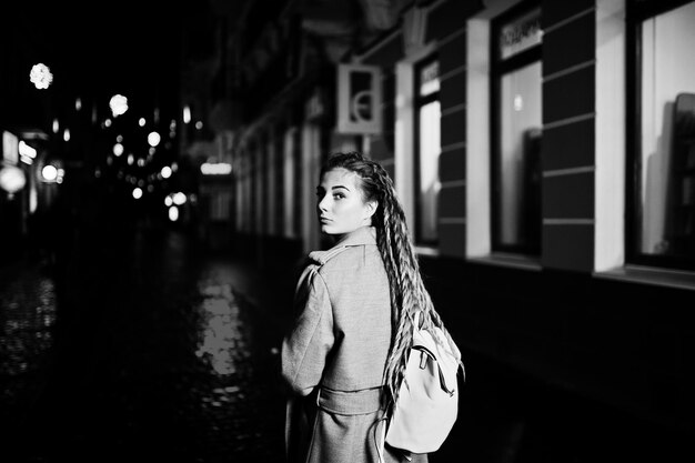 Chica con rastas caminando por la calle nocturna de la ciudad