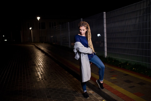 Chica con rastas caminando por la calle nocturna de la ciudad