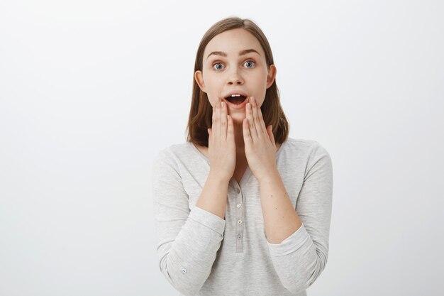 Chica reaccionando ante una asombrosa sorpresa, complacida y encantada, afortunada de tener amigos geniales. Retrato de mujer encantadora con lindo oído movido jadeando de asombro sosteniendo las palmas en el mentón impresionado