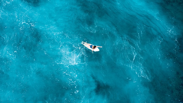 Chica recostada sobre una tabla de surf y flotando en el mar abierto con aguas cristalinas en Maldivas