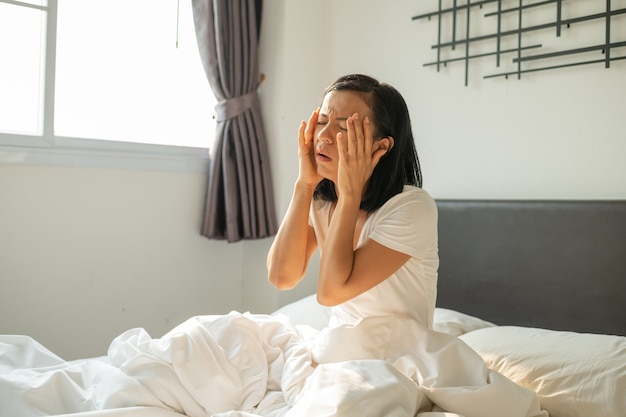 Chica resaca duerme con dolor de cabeza. mujer infeliz que siente dolor de cabeza después de un despertar repentino por una llamada telefónica, alarma temprano en la mañana, mujer joven agotada que sufre de insomnio o migraña, acostada en la cama