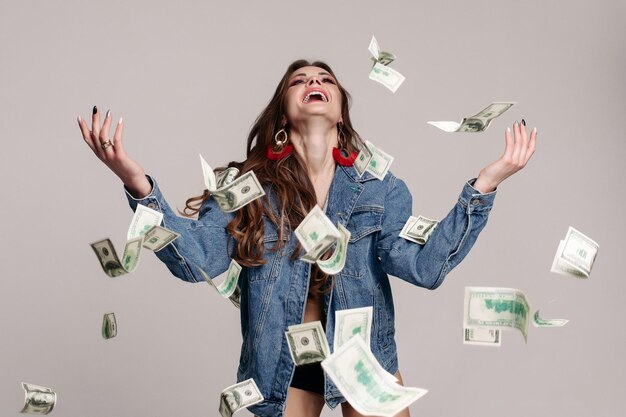 Chica riendo feliz en chaqueta de mezclilla con billetes voladores alrededor