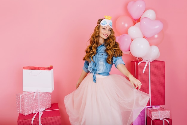 Foto gratuita chica rizada atractiva en moda falda exuberante baila esperando invitados a la fiesta de cumpleaños con regalos en el fondo. adorable joven disfruta de globos y regalos que recibió de amigos