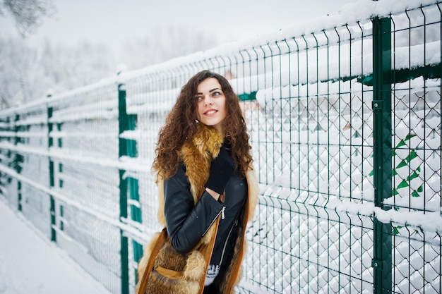 Chica rizada de elegancia en abrigo de piel en el parque forestal nevado en invierno