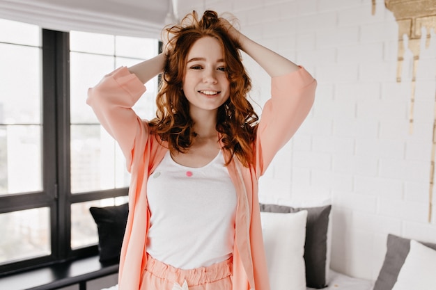 Chica rizada de moda sonriendo en la mañana. Señora blanca alegre posando en casa.