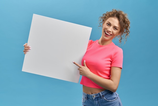 Chica rizada sonriendo sosteniendo tablero blanco