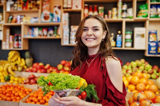 Chica de rojo con diferentes verduras en la tienda de frutas