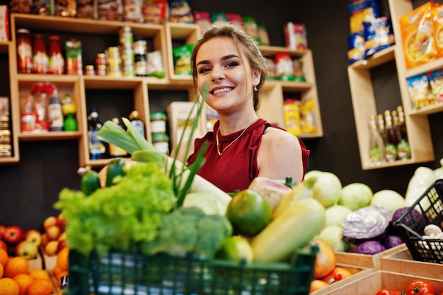 Chica de rojo con diferentes verduras en la tienda de frutas