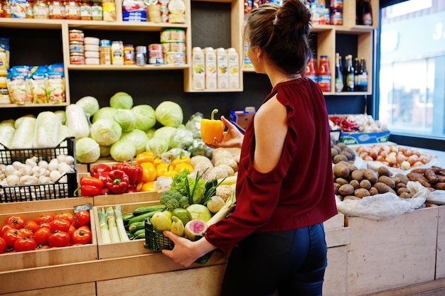 Chica de rojo con diferentes verduras en la tienda de frutas