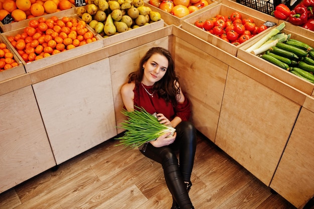 Foto gratuita chica de rojo sosteniendo cebollas verdes en la tienda de frutas