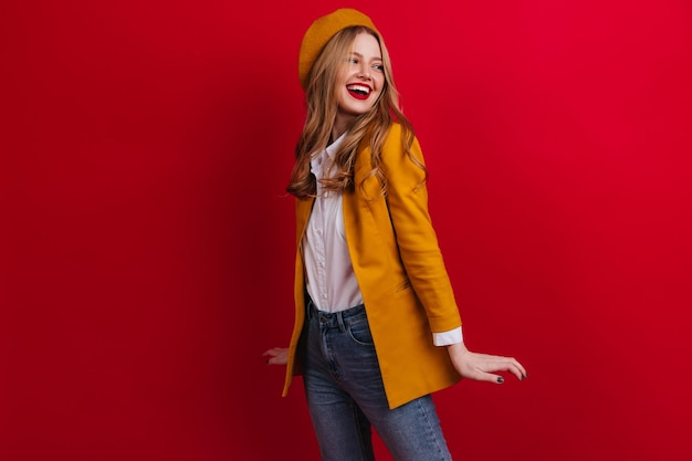 Chica romántica en traje amarillo posando con sonrisa Foto de estudio de adorable dama francesa aislada sobre fondo rojo