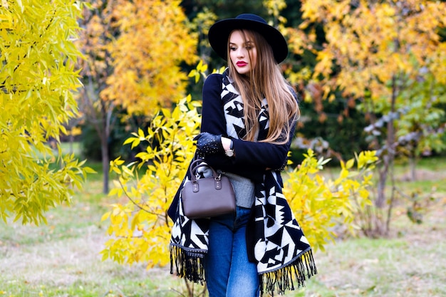 Foto gratuita chica romántica en vasos con sombrero y posando con expresión de cara de besos de pie en medio del parque. retrato al aire libre de linda mujer joven con bufanda de moda divirtiéndose durante la caminata en el bosque.