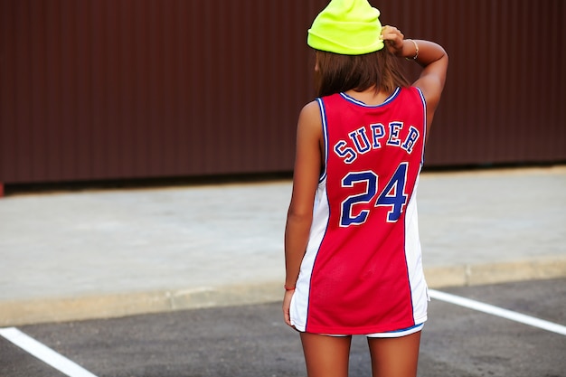 Chica en ropa deportiva de baloncesto rojo sentado sobre asfalto