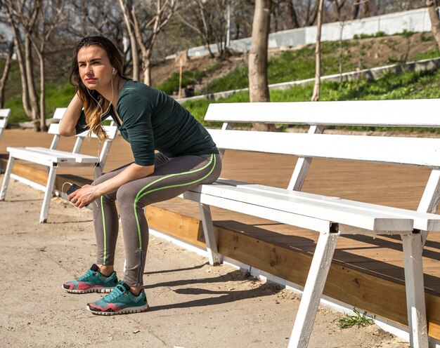 La chica en ropa deportiva en un banco escuchando música