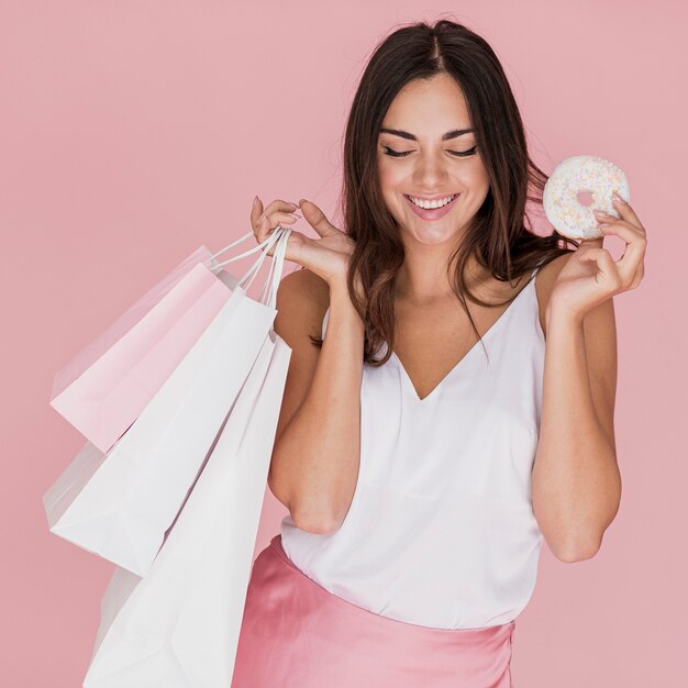 Chica con una rosquilla y bolsas de compras sobre fondo rosa