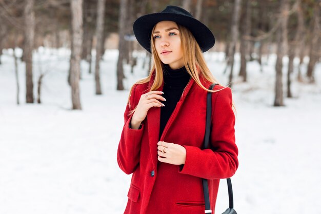 Chica rubia con abrigo rojo en un campo cubierto de nieve