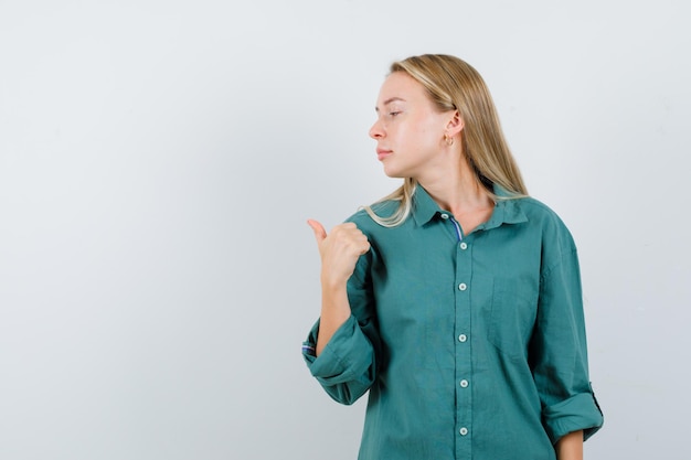 Chica rubia apuntando a la izquierda en blusa verde y luciendo radiante