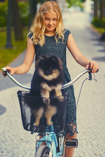 Chica rubia en bicicleta y un perro Spitz en una canasta.