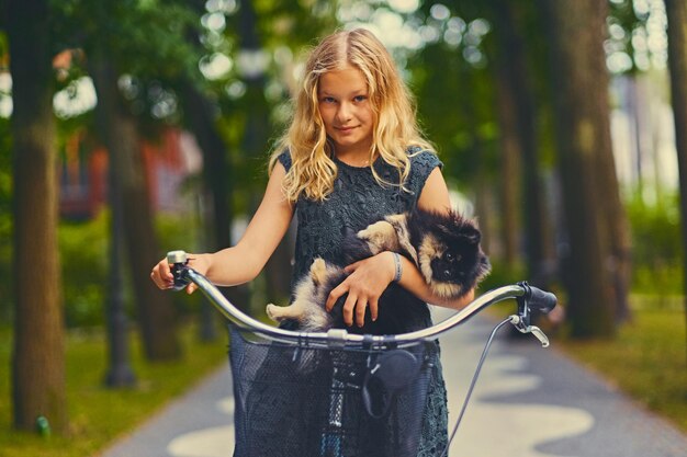 Chica rubia en bicicleta y un perro Spitz en una canasta.