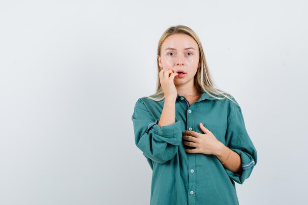 Chica rubia en blusa verde mordiendo el dedo mientras sostiene la mano en el pecho y parece emocionado