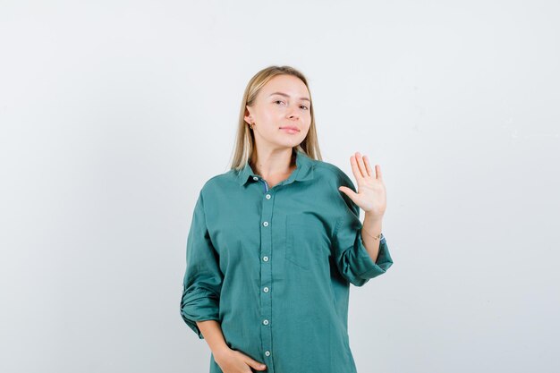 Chica rubia en blusa verde que muestra la señal de pare mientras sostiene la mano en el vientre y se ve bonita