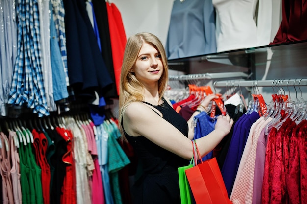 Chica rubia con bolsas de compras elige ropa en la boutique