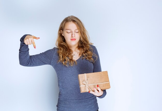 Chica rubia con una caja de regalo de cartón apuntando hacia abajo.