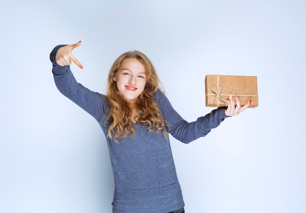 Chica rubia con una caja de regalo de cartón apuntando hacia abajo.