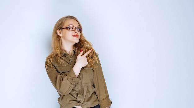 Chica rubia con camisa verde apuntando hacia arriba.