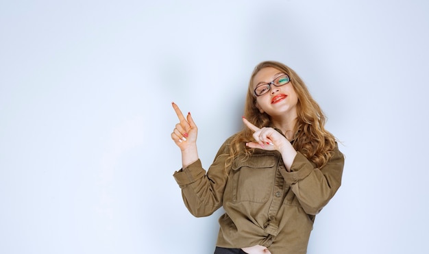 Foto gratuita chica rubia con camisa verde apuntando hacia arriba.