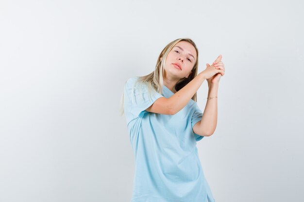 Chica rubia en camiseta azul mostrando gesto de pistola y mirando confiado, vista frontal.