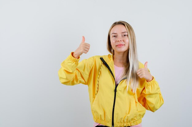 Chica rubia en camiseta, chaqueta mostrando doble pulgar hacia arriba y mirando alegre