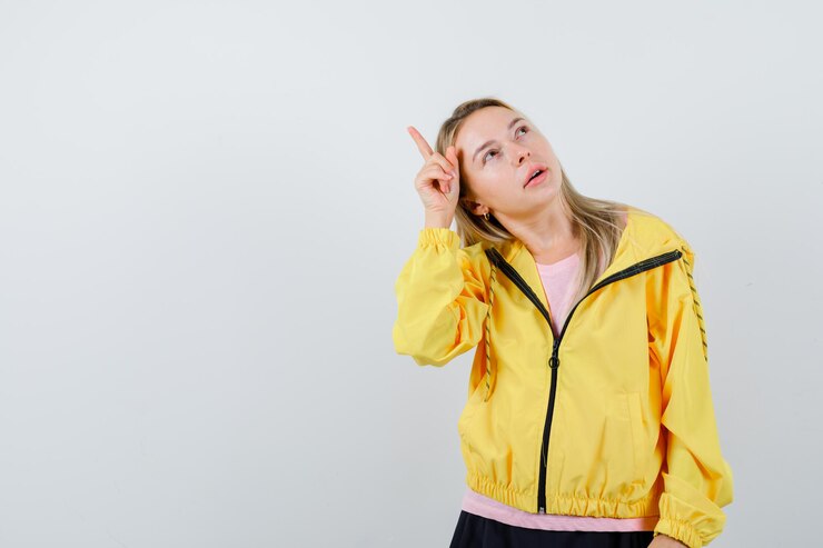 Foto gratuito chica rubia en camiseta rosa y chaqueta amarilla levantando el dedo índice por encima de la cabeza en gesto eureka y mirando pensativo