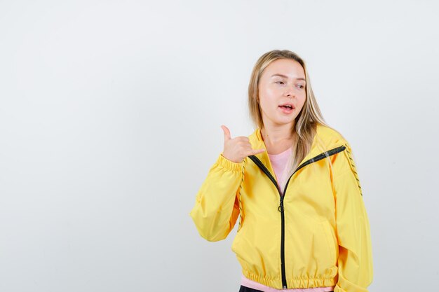 Chica rubia en camiseta rosa y chaqueta amarilla mostrando el pulgar hacia arriba, mirando a otro lado y mirando pensativo