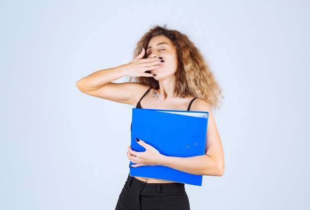 La chica rubia con una carpeta azul parece somnolienta y cansada.