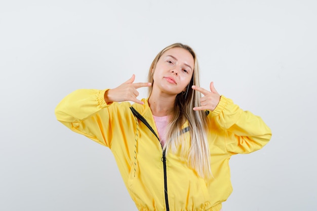 Chica rubia en chaqueta amarilla haciendo símbolo de rock y luciendo elegante