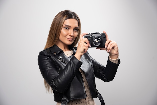 Chica rubia con chaqueta de cuero negro tomando sus selfies con una cámara.