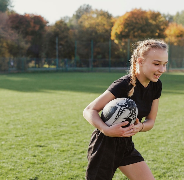 Chica rubia corriendo con una pelota de rugby