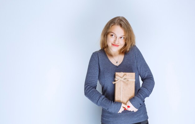 Chica rubia demostrando su caja de regalo de cartón y sintiéndose positiva.